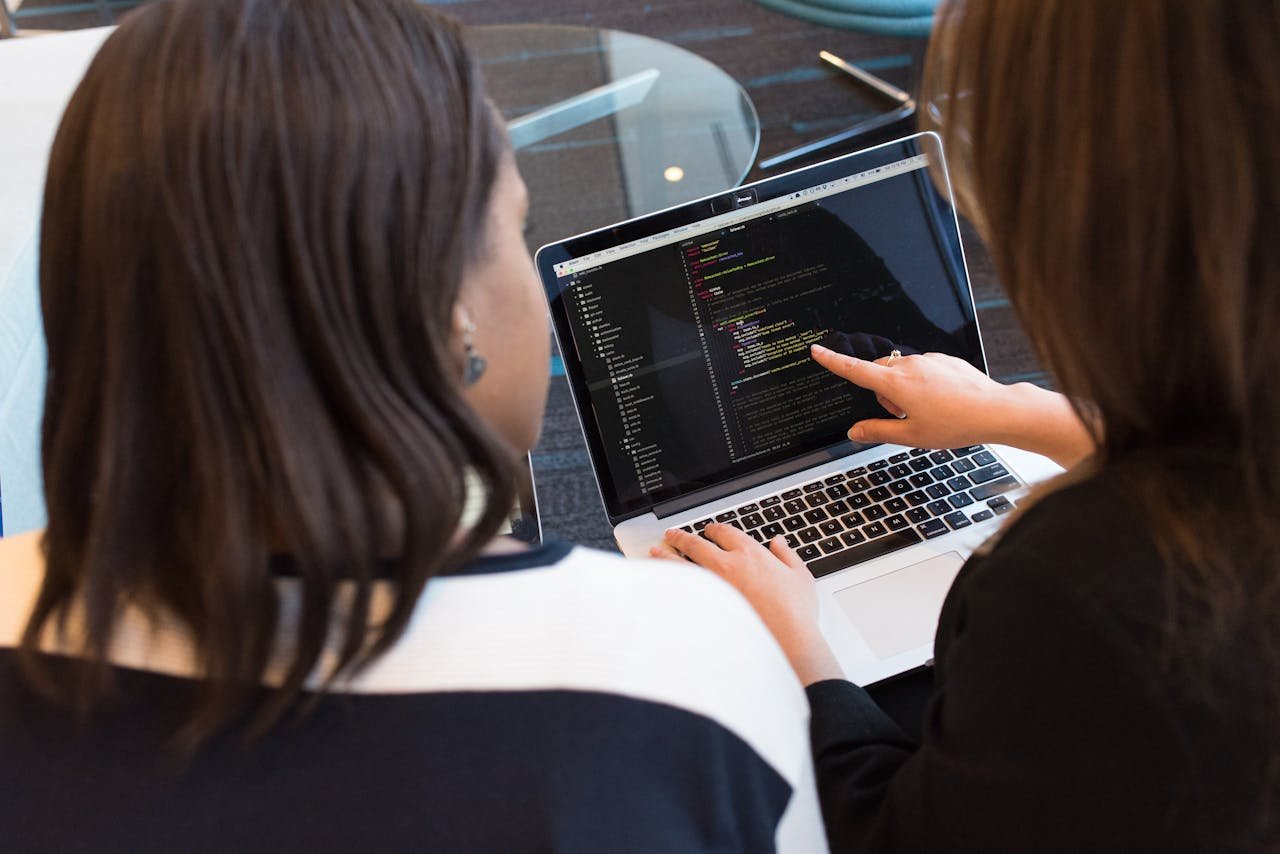 Crafting Captivating Headlines: Your awesome post title goes here Two women working together on software programming indoors, focusing on code.