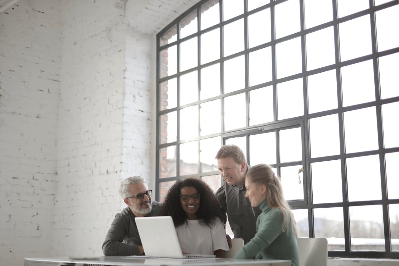 Group of colleagues collaborating around a laptop in a bright, modern office space.